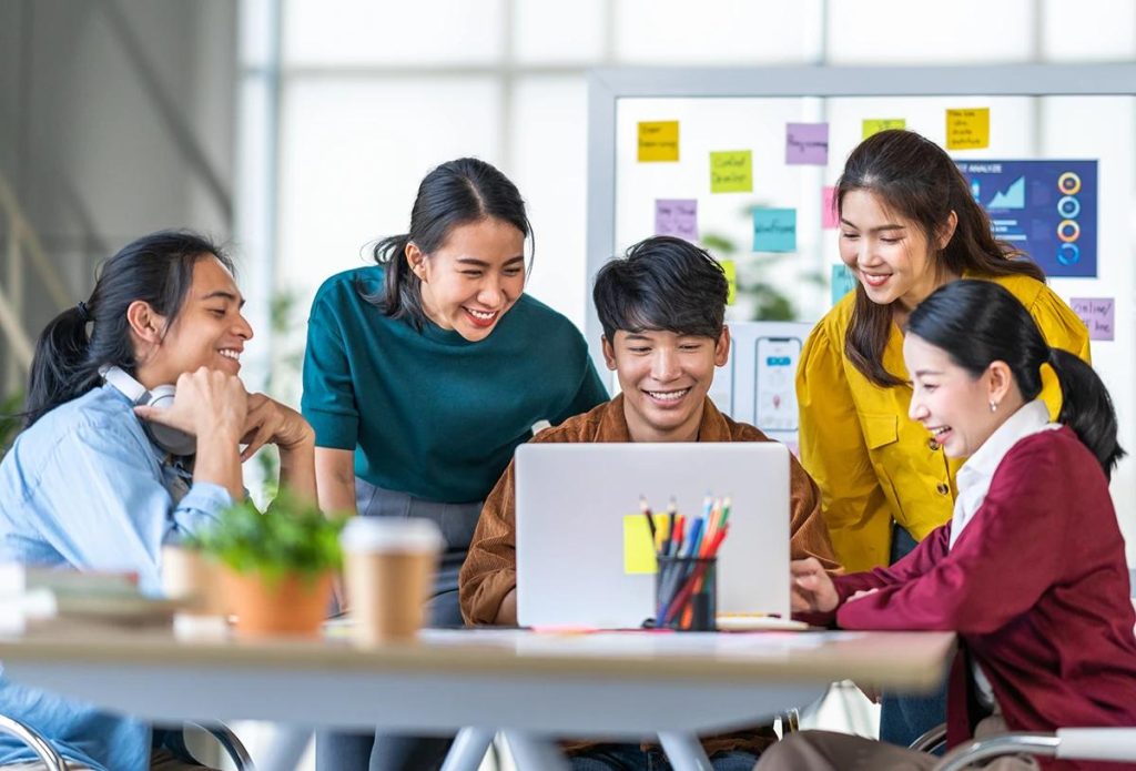 Filipino office colleagues collaborating around a laptop in a bright workplace.